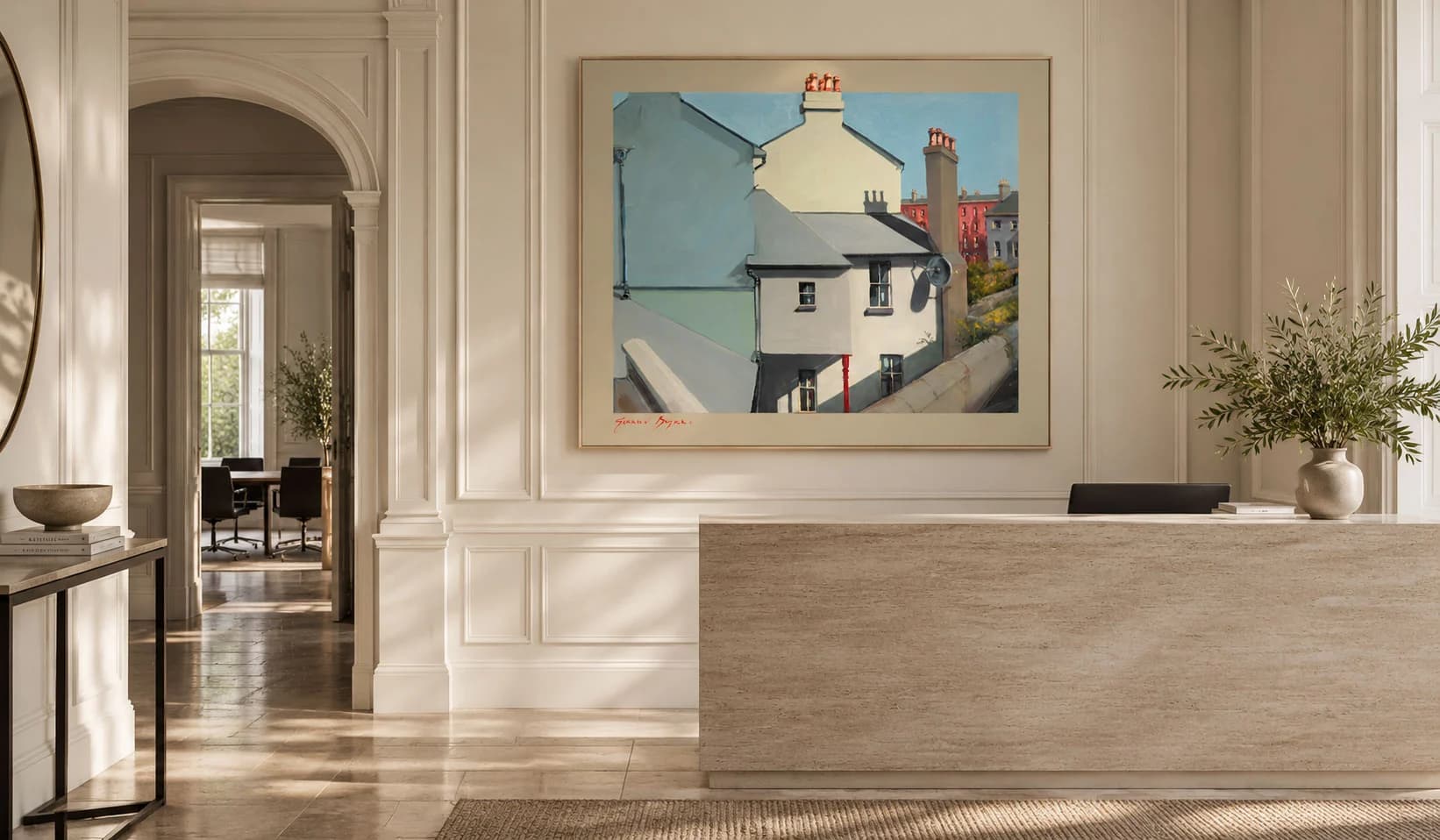 A painting of pale terraced houses and chimney stacks under a blue sky, hung above the stone reception desk of a bright panelled interior.