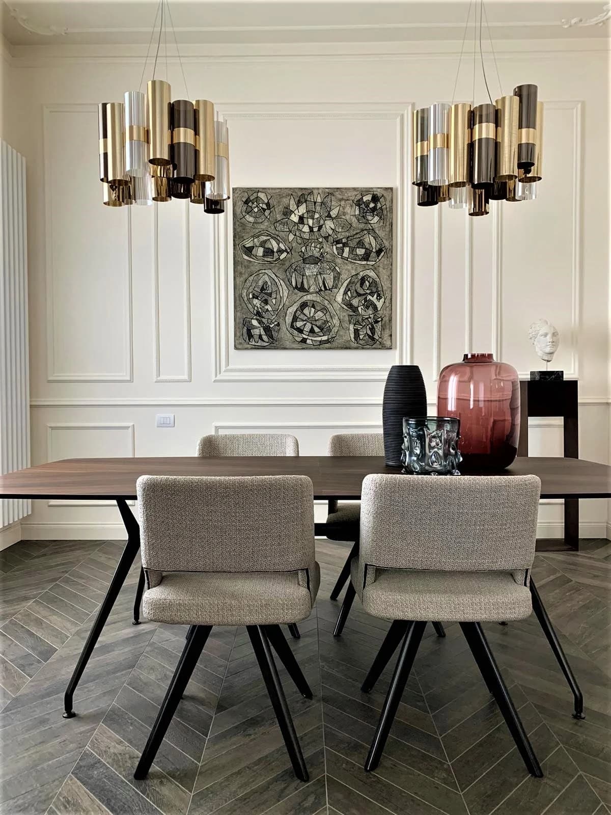 A framed work by Sergi Barnils on a white panelled wall above a dining table, between two brass chandeliers.